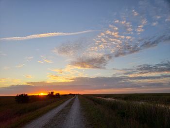 Road amidst field against sky during sunset