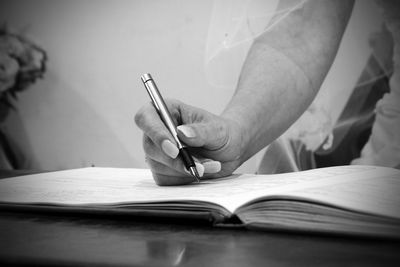 Cropped hand of bride writing on book at table