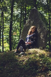 Rear view of woman sitting on tree trunk in forest