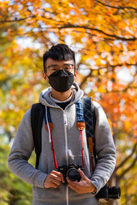 Portrait of young man standing against tree during autumn