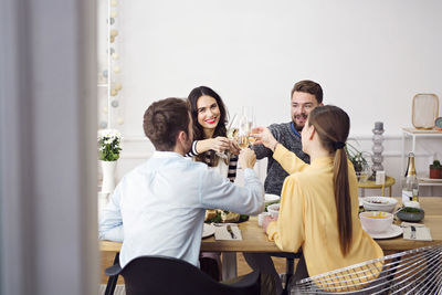 Happy friends toasting champagne flutes while sitting at dinning table in lunch party