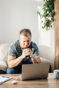 A young pensive male businessman works at home on a laptop, checks mail and calls online 