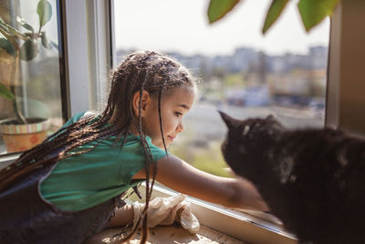 Side view of girl with cat by window