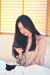 Young woman using phone while sitting on bed