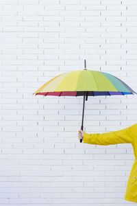 Woman holding multi colored umbrella in front of brick wall