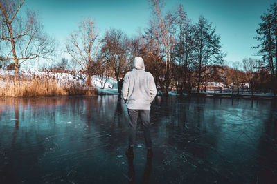 Rear view of man standing by lake against sky during winter