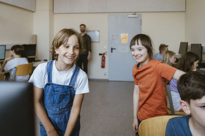 Happy girl having fun with disabled female friend in computer classroom at school