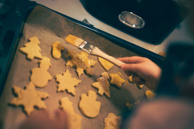 Child coating christmas cookies on a baking sheet with egg yolk.