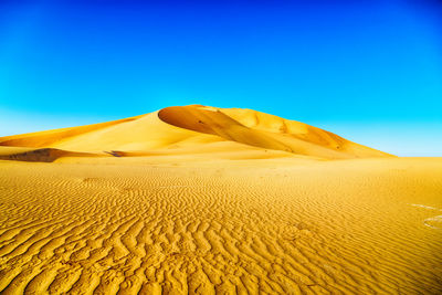 Sand dunes in desert against clear blue sky