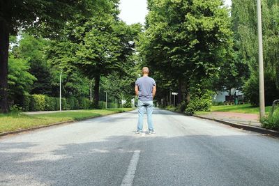 Rear view of man on road amidst trees in city