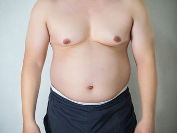 Midsection of shirtless man standing against wall