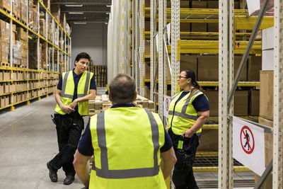 Multi-ethnic coworkers discussing while standing by racks at distribution warehouse