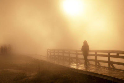 Silhouette man standing on railing against sky during sunset