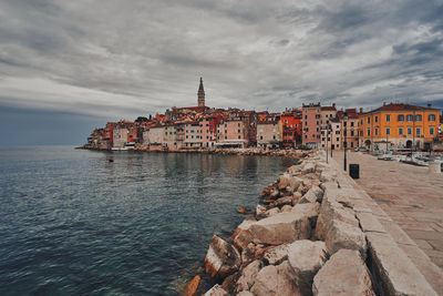 Buildings by sea against cloudy sky