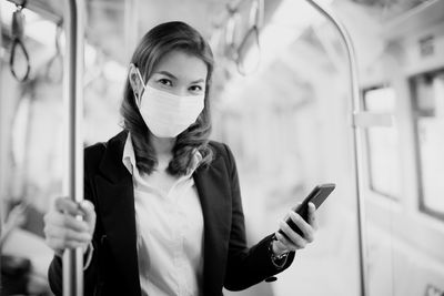 Portrait woman wearing mask using smart phone standing in train