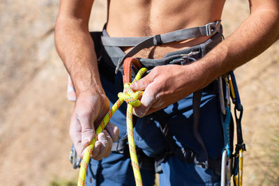 Midsection of shirtless man wearing safety harness while standing outdoors