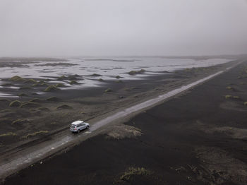 Aerial of car driving down sandy gravel road near stokksnes, ice