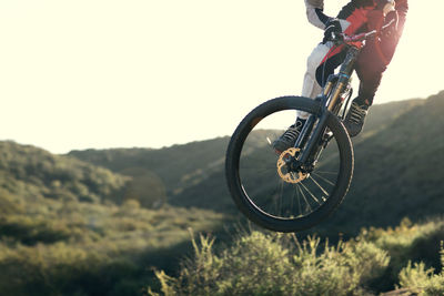 Low section of mountain biker in mid-air over mountain against clear sky