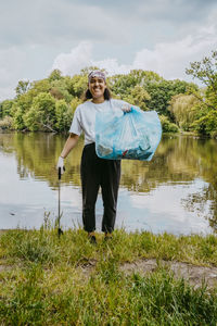 Portrait of smiling female environmentalist with plastic bag against pond