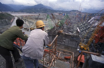 Rear view of people looking at construction site against sky