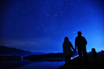 Silhouette couple standing against star field in sky at night