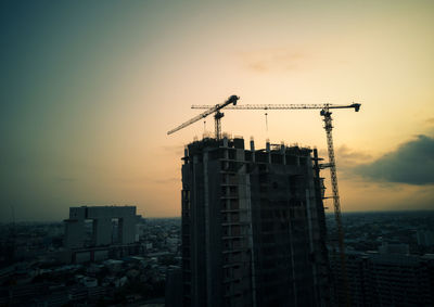 Silhouette crane by building against sky during sunset