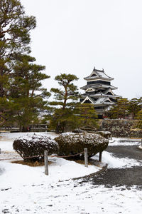 Gazebo on snow covered field by building against sky