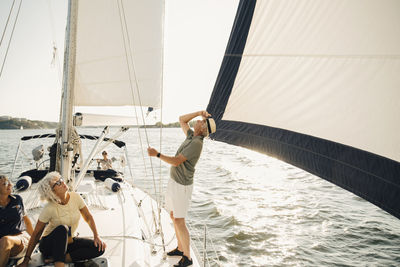 Senior man looking up while standing by female friends in boat on sunny day