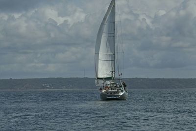 Boats sailing in sea against cloudy sky