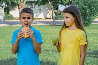 Teenage boy and girl with apple and burger in the park. choice between healthy and unhealthy food.