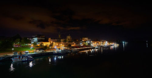 Illuminated buildings by river against sky at night