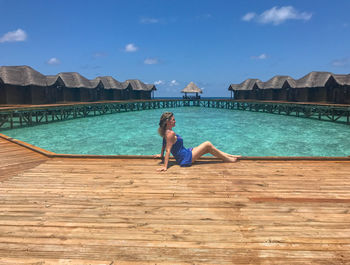 Woman sitting by swimming pool against sky