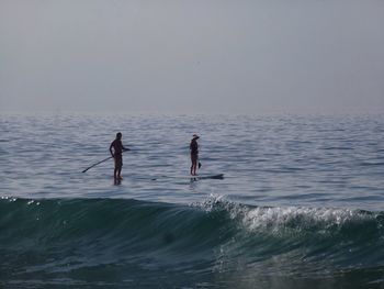 People paddleboarding on sea against clear sky