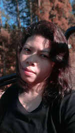 Close-up portrait of beautiful young woman sitting against trees