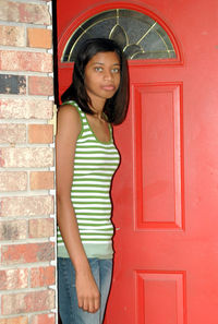 Portrait of young woman standing against door