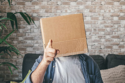 Man gesturing while covering face with cardboard box at home