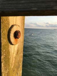 Close-up of wooden post by sea against sky