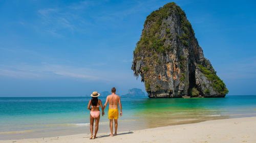 Rear view of woman standing at beach against sky