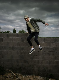 Full length of man jumping from wall against cloudy sky