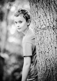 Portrait of teenage boy standing against tree trunk