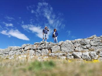 Low angle view of men standing on rock against blue sky