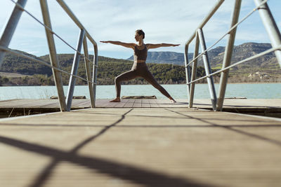 Sportswoman doing warrior 2 pose on jetty during sunny day