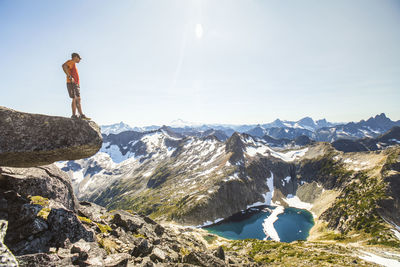 Hiker looks down at view of lake and peaks from mountain summit