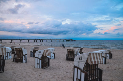 Hooded chairs at beach against sky during sunset