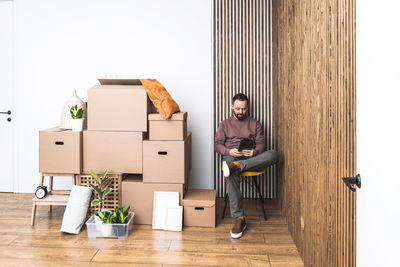 Mature man using his tablet, unpacking things from boxes while moving in new unfurnished apartment.