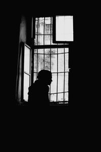 Silhouette man looking through window