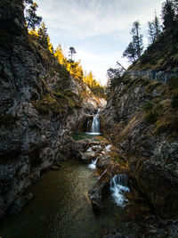 Stream flowing through rocks against sky