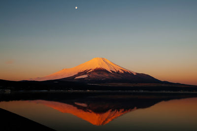 Reflection of snowcapped mountains in river against clear sky at dusk