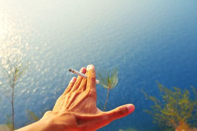 Cropped hand of man holding cigarette over sea