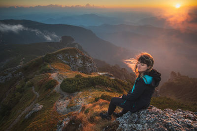 Man sitting on rock looking at mountain during sunset